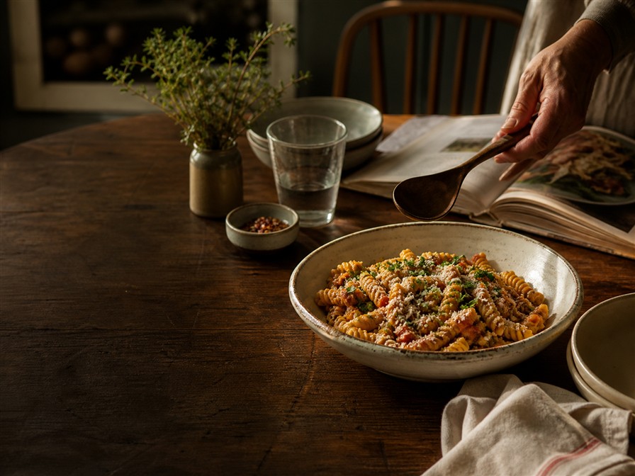 Rustic pasta on a warm wooden table beside an open cookbook