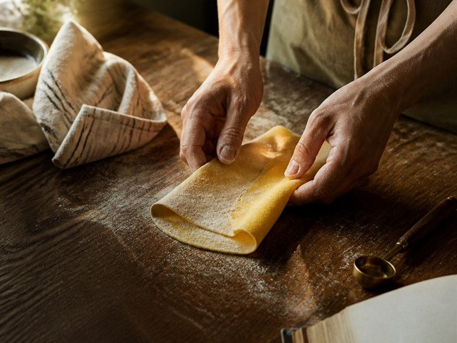 Hands folding fresh pasta dough on a wooden kitchen table
